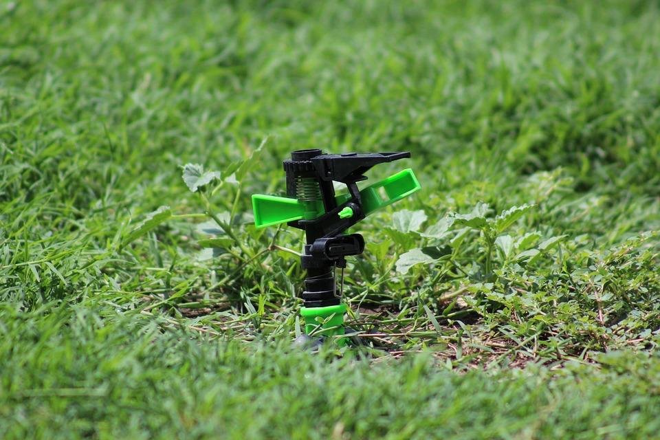 Close-up of a green and black sprinkler head in a lush green lawn, showcasing the efficiency of irrigation systems for maintaining healthy grass.